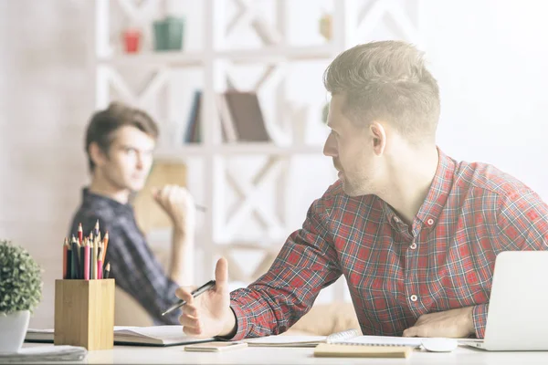 Retrato de homem branco bonito escrevendo no bloco de notas e conversando com colega no local de trabalho. Conceito de papelada — Fotografia de Stock