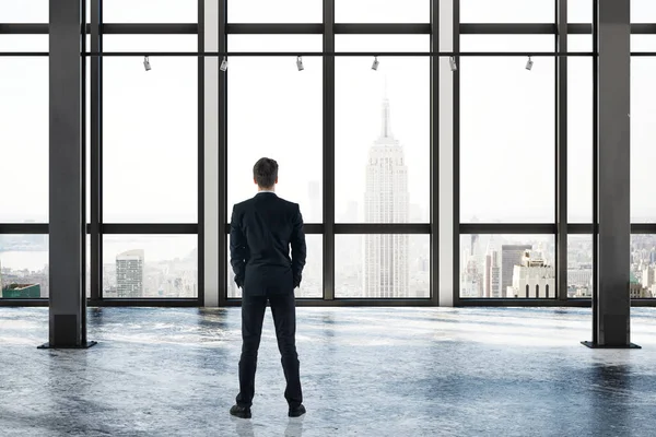 Vista trasera del joven hombre de negocios en el interior de la habitación de hormigón vacío con vista a la ciudad de Nueva York y la luz del día. Concepto de investigación. Renderizado 3D — Foto de Stock