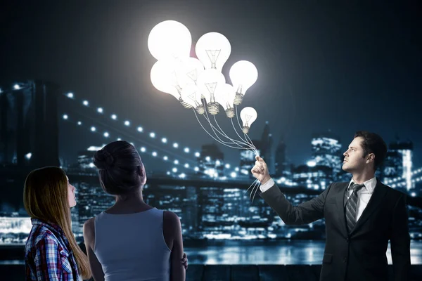 Empresario y mujeres jóvenes sosteniendo globos abstractos de lámparas brillantes sobre un fondo borroso de la ciudad nocturna. Concepto de imaginación —  Fotos de Stock