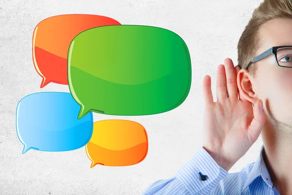 Young businessman listening carefull on concrete wall background with empty speech bubbles. Commuication concept. Mock up — Stock Photo, Image