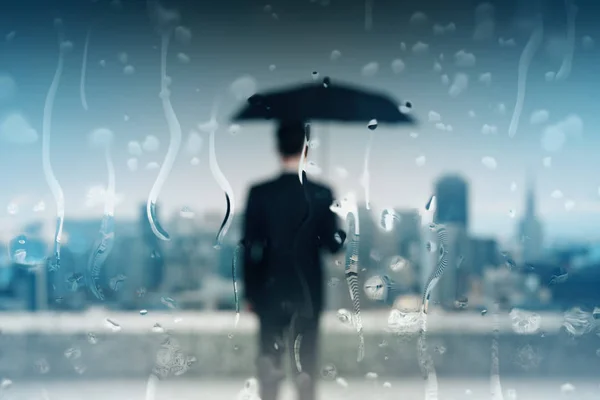 Back view of blurry young businessman with umbrella on roof top with rain drops. Safety concept — ストック写真