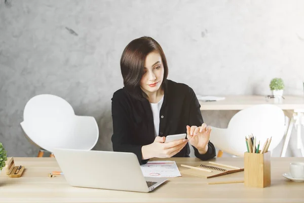 Attraktiva affärskvinna med smartphone på arbetsplatsen — Stockfoto