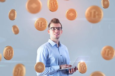Düşme ile gri arka plan üstünde laptop altın bitcoins kullanarak çekici gülümseyen genç Avrupa iş adamı. Internet ve para kavramı