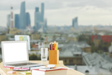 Modern masaüstü boş beyaz dizüstü, sarf malzemeleri ve diğer öğeler bulanık şehir görünümü arka plan üzerinde ile kapatın. Yukarı alay 