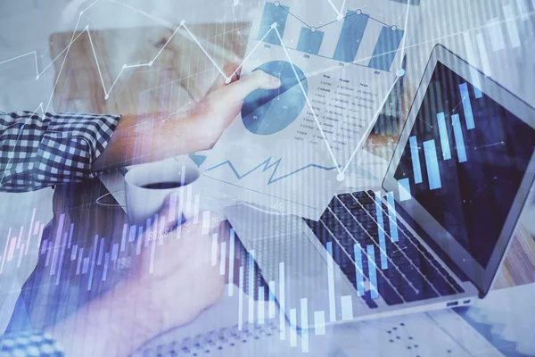 Double exposure of businessmans hands with laptop and stock market graph background. Concept of research and trading.