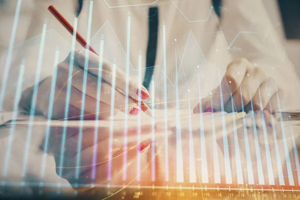 A woman hands writing information about stock market in notepad. Forex chart holograms in front. Concept of research.