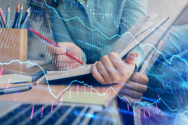 Una mujer escribe información sobre el mercado de valores en bloc de notas. Hologramas gráfico de divisas en frente. Concepto de investigación. Exposición múltiple — Foto de Stock