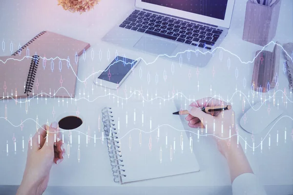 Manos escribiendo información sobre el mercado de valores en bloc de notas. Hologramas gráfico de divisas en frente. Concepto de investigación. Exposición múltiple —  Fotos de Stock