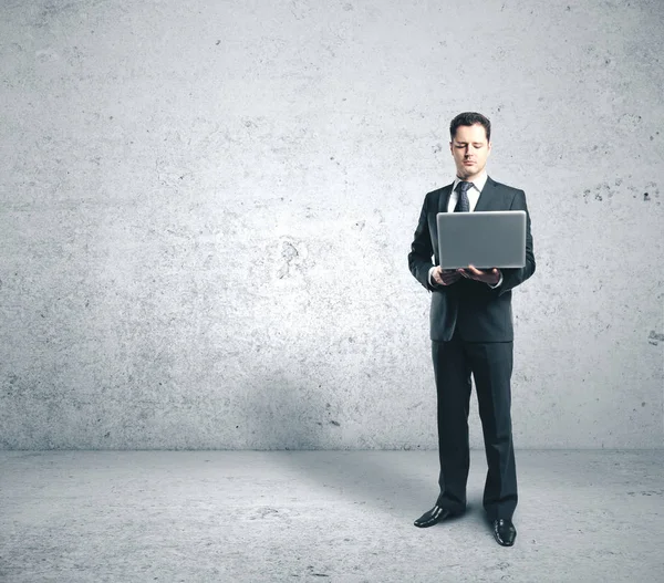 Businessman in suit holding laptop cocrete interior. — Stock Photo, Image