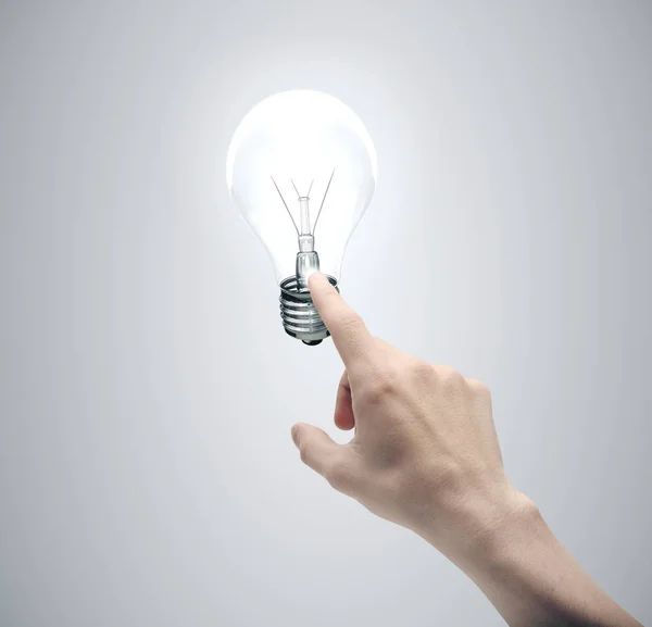 Hand pushing light bulb on gray background. — Stock Photo, Image