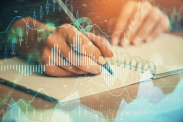 Forex graph on hand taking notes background. Concept of research. Double exposure