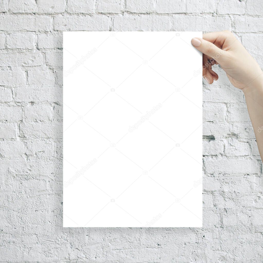 Hand holding white blank poster on brick wall background. Presentation concept.
