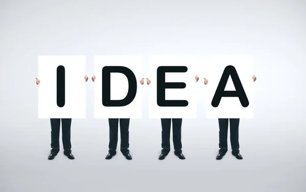 Vier Geschäftsleute Halten Ein Weißes Plakat Mit Ideensymbol Der Hand — Stockfoto
