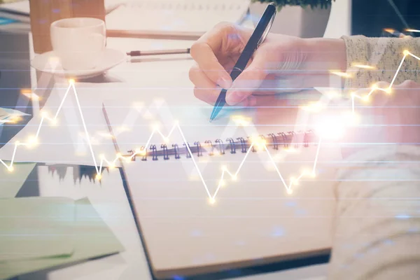 Hand taking notes in notepad. Forex chart holograms in front. Concept of research. Double exposure