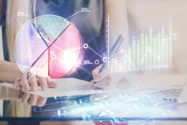 Una mujer escribe información sobre el mercado de valores en bloc de notas. Hologramas gráfico de divisas en frente. Concepto de investigación . —  Fotos de Stock