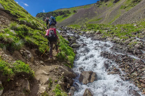 Los turistas de montaña suben la colina a lo largo del río turbulento en las montañas del Cáucaso — Foto de Stock