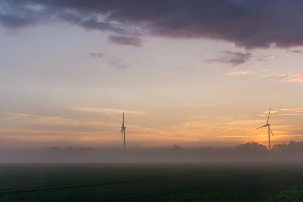 Windräder bei Sonnenaufgang und Nebel mit dunklen Wolken — Stockfoto