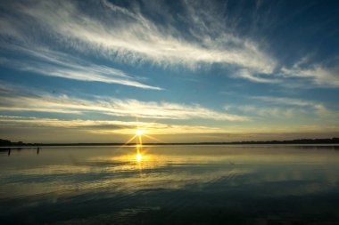 Gündoğumu ile beyaz bulutlar dalgalar olmadan bir gölde