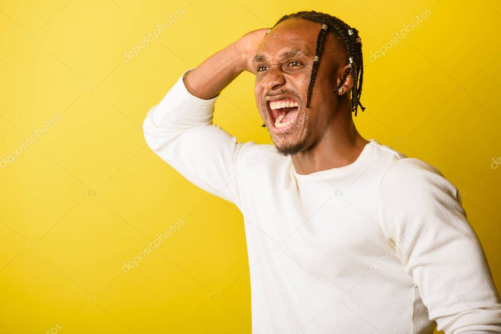 portrait of a young black man, african appearance, emotional and serious and looking upwards, flailing his hands, from dreadlocks, against yellow background 