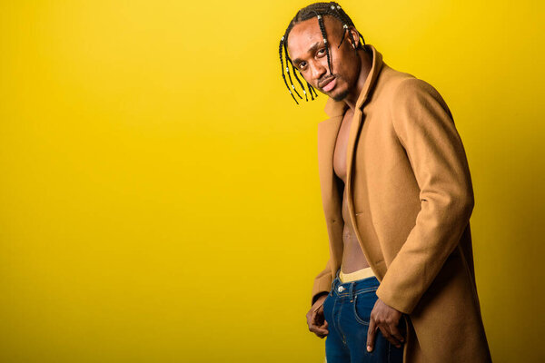 portrait of young black man, african appearance, emotional and serious and looking straight, with dreadlocks, against yellow background 