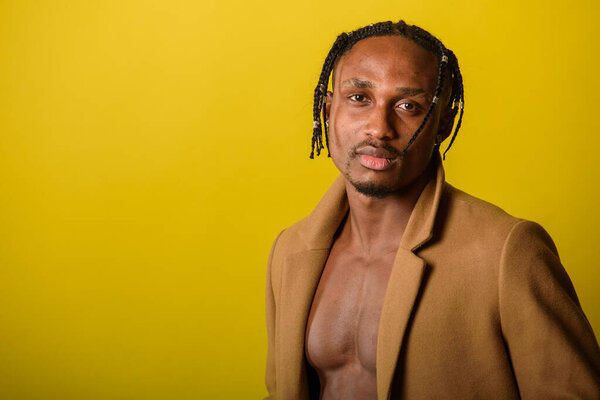 portrait of young black man, african appearance, emotional and serious and looking straight, with dreadlocks, against yellow background 