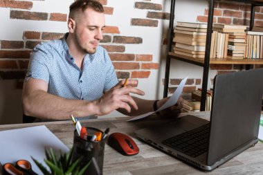 Modern bir ışık dolabında belgeleri olan genç bir Avrupalı bilgisayar başında çalışıyor. Endişeli, iş için endişeli. Bilgisayarla ilgili düşünceli bir çalışan, kopyalama alanı, bilgisayara bakıyor