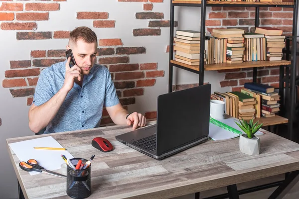 A young European man working at a computer with documents in a modern light cabinet. worried, worried about the job. Thoughtful employee at work with computer, copy space, looks at computer