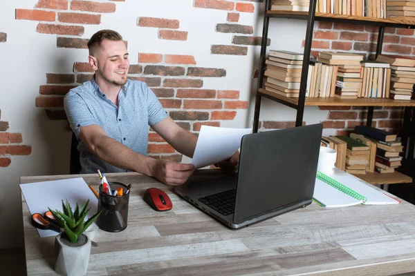 A young European man working at a computer with documents in a modern light cabinet. worried, worried about the job. Thoughtful employee at work with computer, copy space, looks at computer