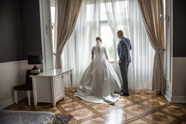 Pencerenin önünde bekleyen güzel bir çift. Koyu kırmızı arka planda gelin ve damadın siluetleri. Düğün sabahı romantik bir randevu.. 