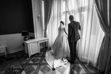 Pencerenin önünde bekleyen güzel bir çift. Koyu kırmızı arka planda gelin ve damadın siluetleri. Düğün sabahı romantik bir randevu.. 