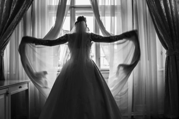 豪華な白いドレスを着た花嫁が美しいホールの窓のそばに立っています 光を制御する — ストック写真