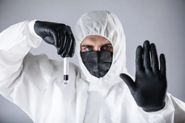 a virologist in a black mask and medical gloves wearing a white protective suit, conducts blood tests and samples for coronavirus, tests. Pandemic. Isolated and in a panic because of the epidemic.