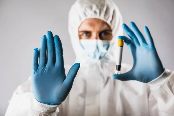 A virologist in a medical mask and protective clothing holds a test tube with a blood sample for coronavirus testing. Pandemic. Respiratory syndrome, panic, experiences, research