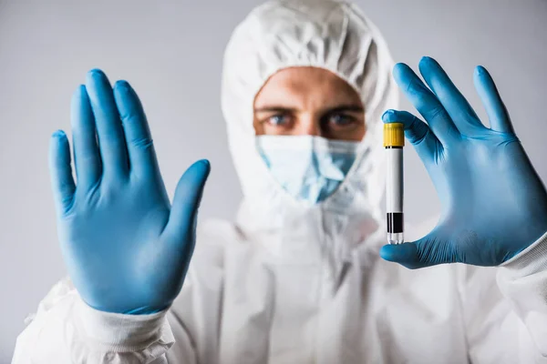 A virologist in a medical mask and protective clothing holds a test tube with a blood sample for coronavirus testing. Pandemic. Respiratory syndrome, panic, experiences, research