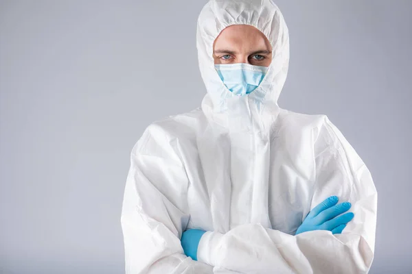 a virologist in a protective suit with a respirator face mask and blue gloves with fear on his face shows cautionary hands with his hands to the camera. collapse of the healthcare system due to the epidemic coronavirus.