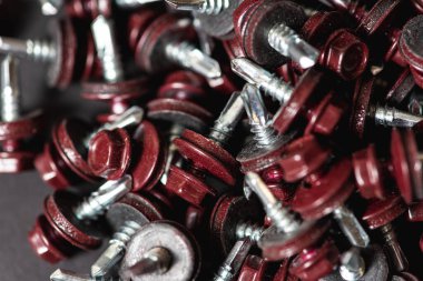 Çatı vidalarının üst görünümü arka plan dokusunu bozar. Kırmızı çatı vidaları arka planda. Çatıyı kızıl saçlılarla onarmak için kendi kendine dokunan vidalar.