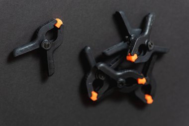 Siyah ve turuncu inşaat klipleri koyu arka plana karşı. Orta boy plastik şarjörler. Joinery için klempleme araçları. Dikiş için el aletleri. Kıskaç ekipmanı