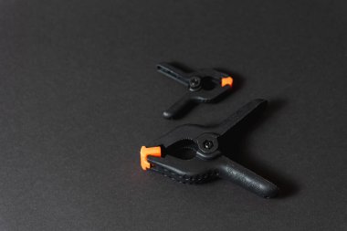 Siyah ve turuncu inşaat klipleri koyu arka plana karşı. Orta boy plastik şarjörler. Joinery için klempleme araçları. Dikiş için el aletleri. Kıskaç ekipmanı