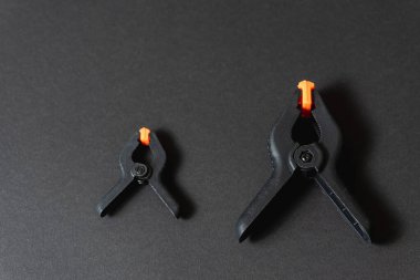 Siyah ve turuncu inşaat klipleri koyu arka plana karşı. Orta boy plastik şarjörler. Joinery için klempleme araçları. Dikiş için el aletleri. Kıskaç ekipmanı