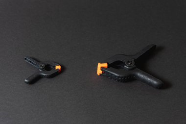 Siyah ve turuncu inşaat klipleri koyu arka plana karşı. Orta boy plastik şarjörler. Joinery için klempleme araçları. Dikiş için el aletleri. Kıskaç ekipmanı