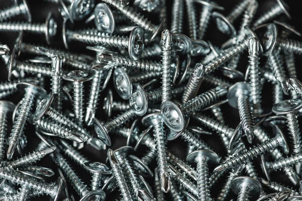 Galvanize vidalar, yarım daire şeklinde bir kafa, haç şeklinde bir delik ve karanlık bir arka planda bir çamaşır makinesi. Kapat.