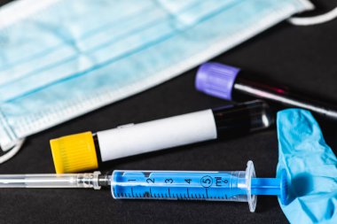 Kan testi tüpü, mavi tek kullanımlık eldivenler, şırınga, tek kullanımlık maske. Kan testi kiti, virüs, salgın hastalık, koruma. Karanlık bir arka planda