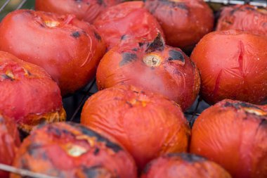 Arka planda ızgarada açık ateşte kızartılmış kırmızı domatesler. Doğada yemek yanıyor.