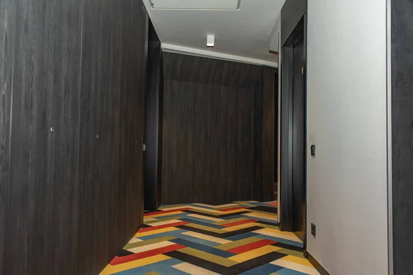 white hallway with many dark brown doors, lanterns and colored carpet