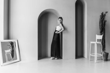 Siyah ve beyaz fotoğraf, geniş bir odada, düşünceli, düşünceli, genç, sarışın ve baştan çıkarıcı bir kızın portresi.