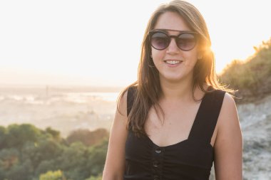 Gündoğumu, sabah, genç, güzel, duygusal, seksi kız kot ceketli ve gözlüklü doğada ahşap bir korkuluğun yanında duruyor.