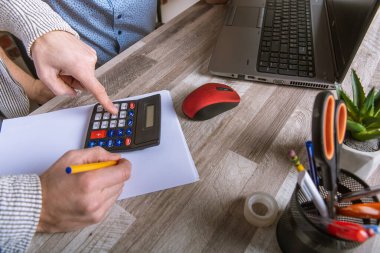 Boş deftere yazı yazan işadamının eli masa, bilgisayar ve hesap makinesine yakın plan