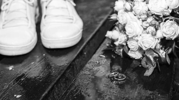 결혼반지와 꽃다발 표면에 있습니다 배경에는 젊은이들의 신발이 보이고 내리고 있습니다 — 스톡 사진