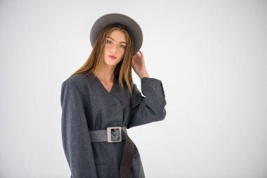 Çekici bir genç kız, gri ceketli bir manken ve elinde bir şapka tutuyor. Erkek tarzı kıyafetler. Beyaz bir arka planda izole edilmiş. Kenarında bir yazı için bir yer var. Seçici odak