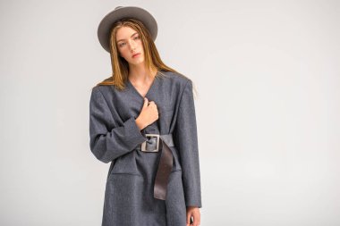 Çekici bir genç kız, gri ceketli bir manken ve elinde bir şapka tutuyor. Erkek tarzı kıyafetler. Beyaz bir arka planda izole edilmiş. Kenarında bir yazı için bir yer var. Seçici odak
